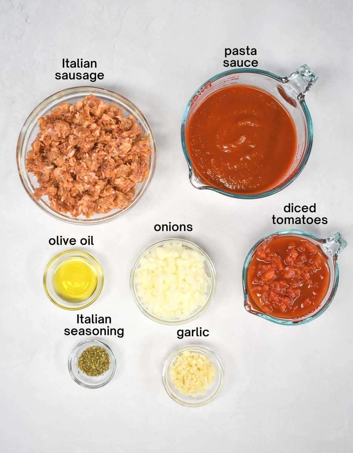 The ingredients for the sauce arranged on a white table with each ingredient labeled in black letters.