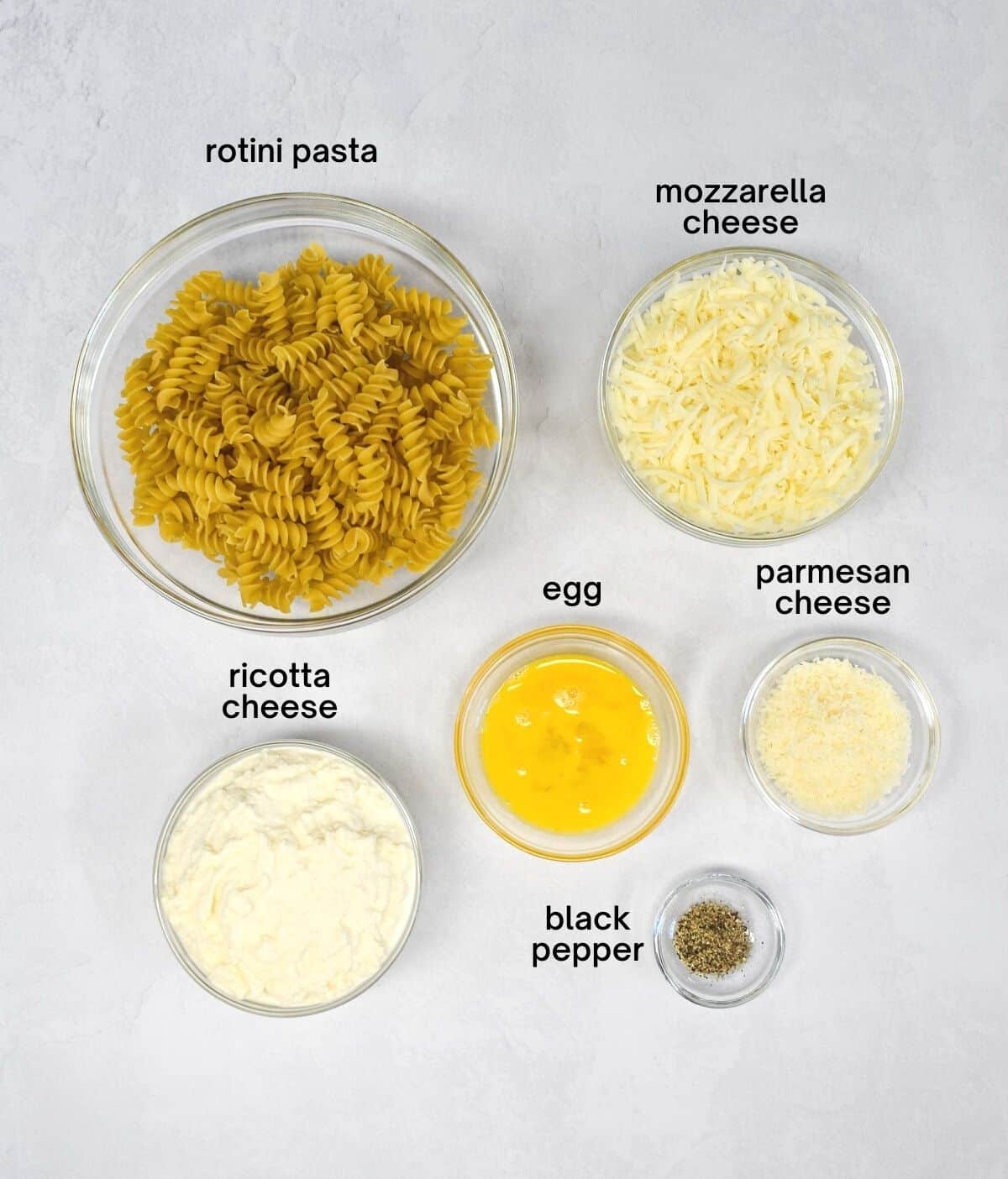 The ingredients for the cheese mixture and the pasta arranged on a white with each ingredient labeled in black letters.