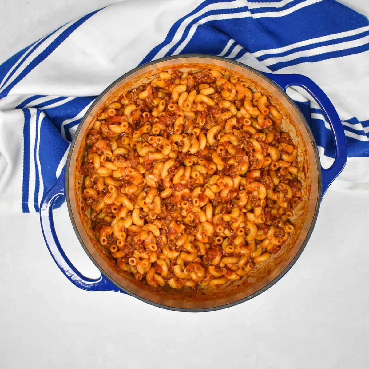 A top image of the beef and macaroni in a large blue pot set on a white table with a blue and white kitchen towel.