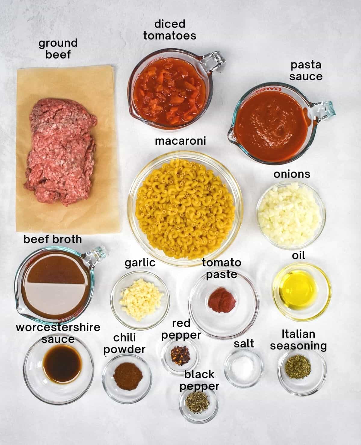 The ingredients for the beefaroni, arranged on a white table with the ingredient name above each in black letters.