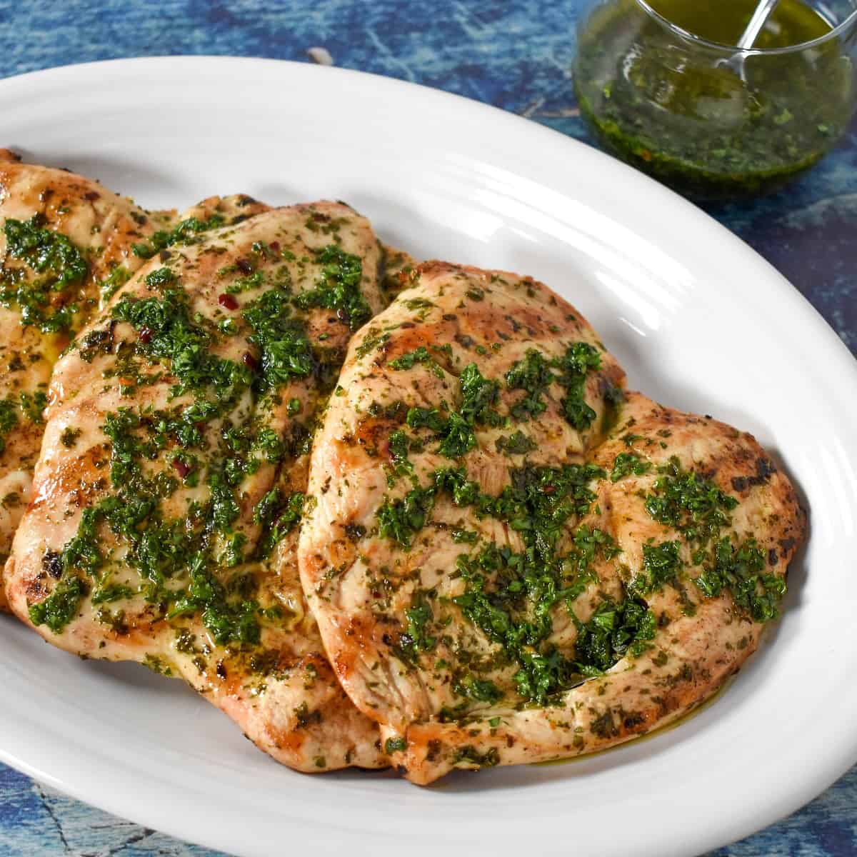 An image of the grilled chicken breast topped with chimichurri and set on a white platter.
