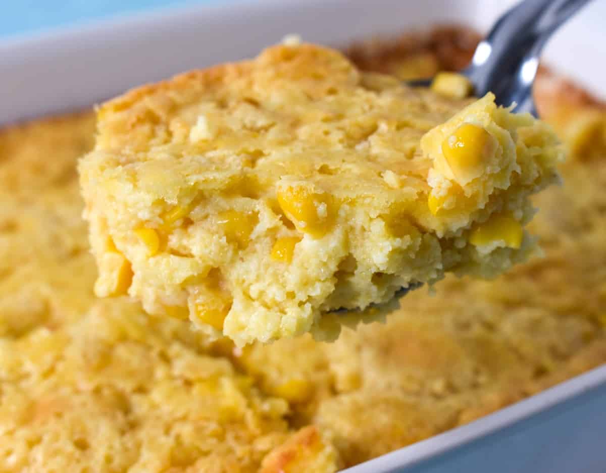 An image of a serving spoon of the corn casserole lifted over the baking dish.
