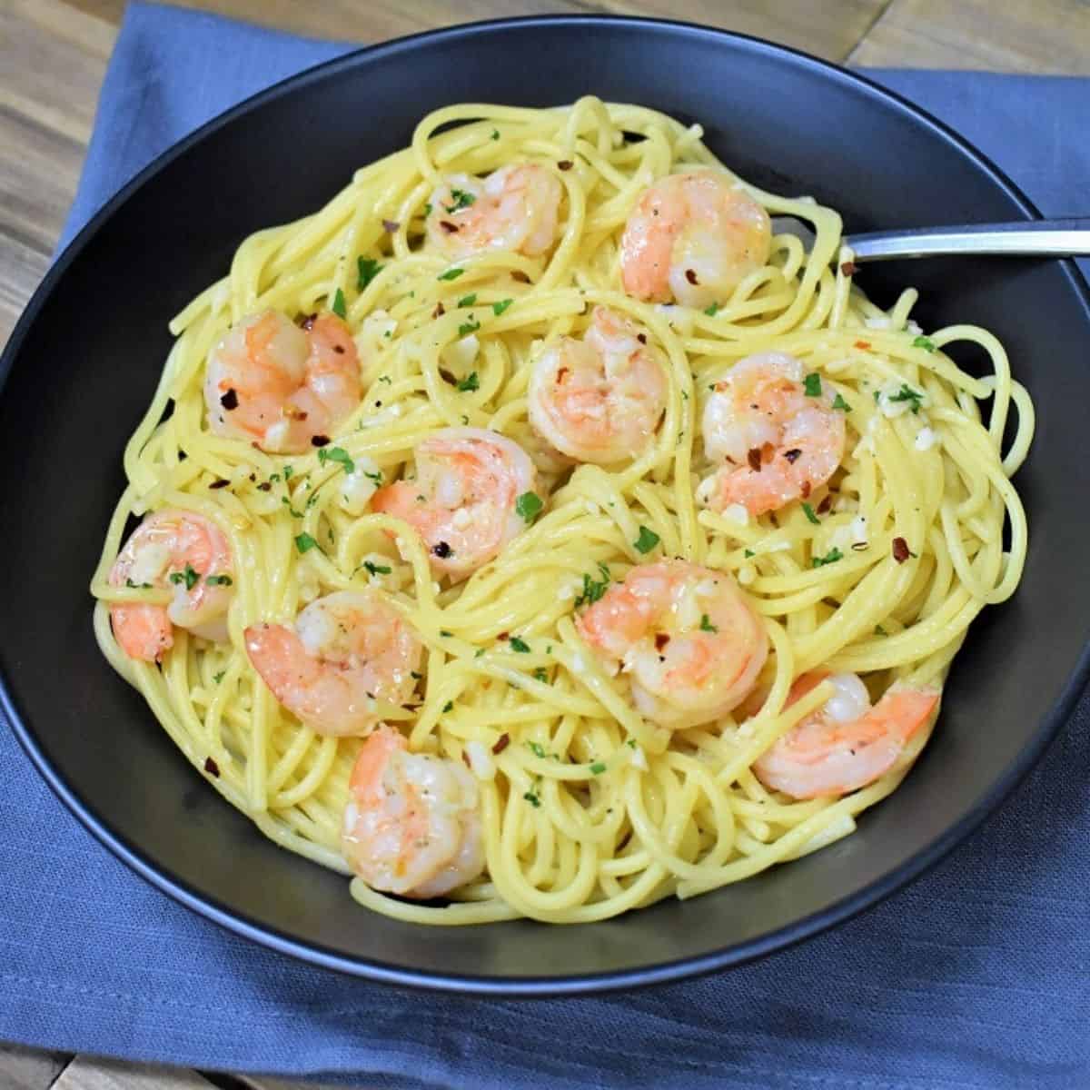 Spaghetti topped with shrimp in an oil and garlic sauce, garnished with parsley and served in a large black bowl.