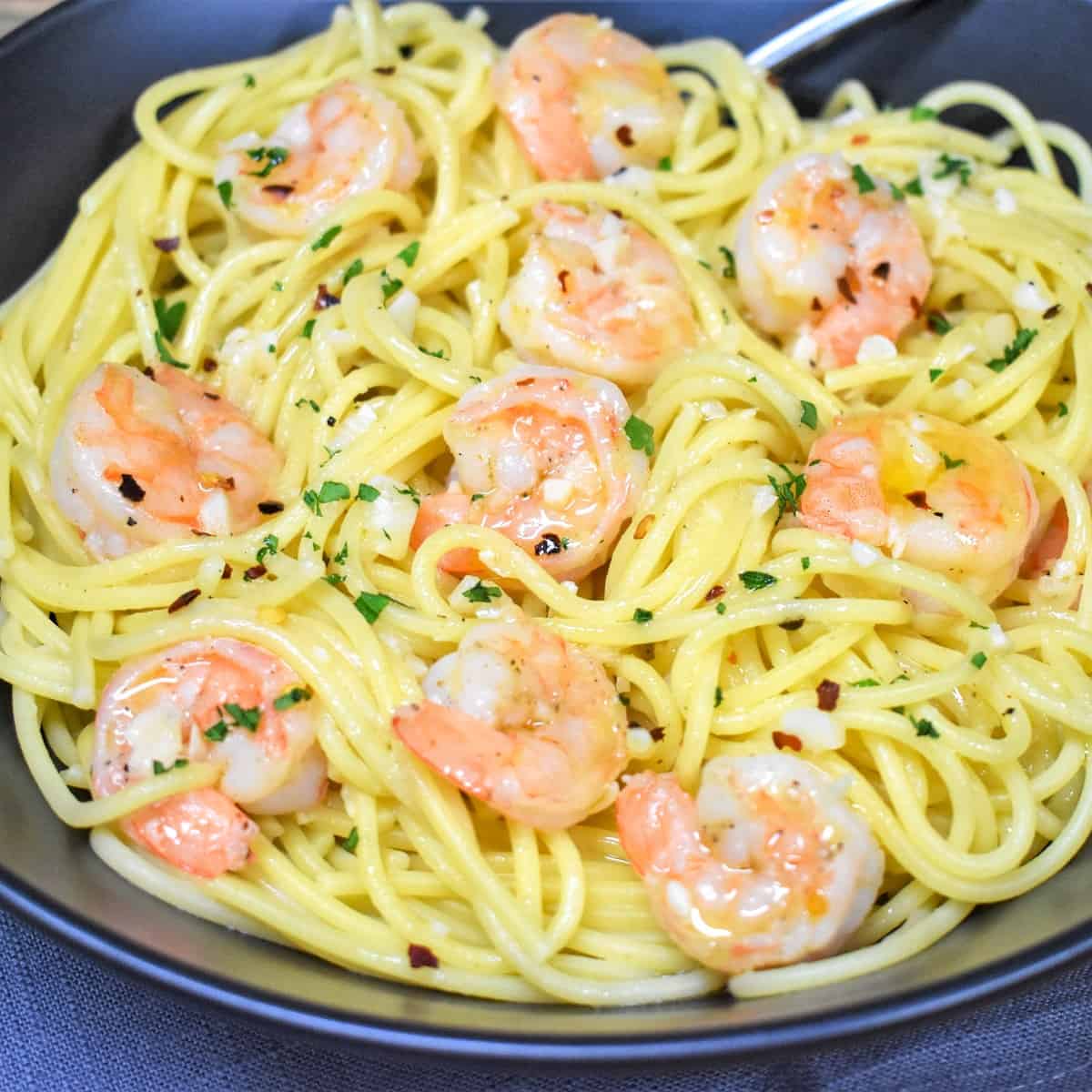 Spaghetti topped with shrimp in an oil and garlic sauce, garnished with parsley and served in a large black bowl.