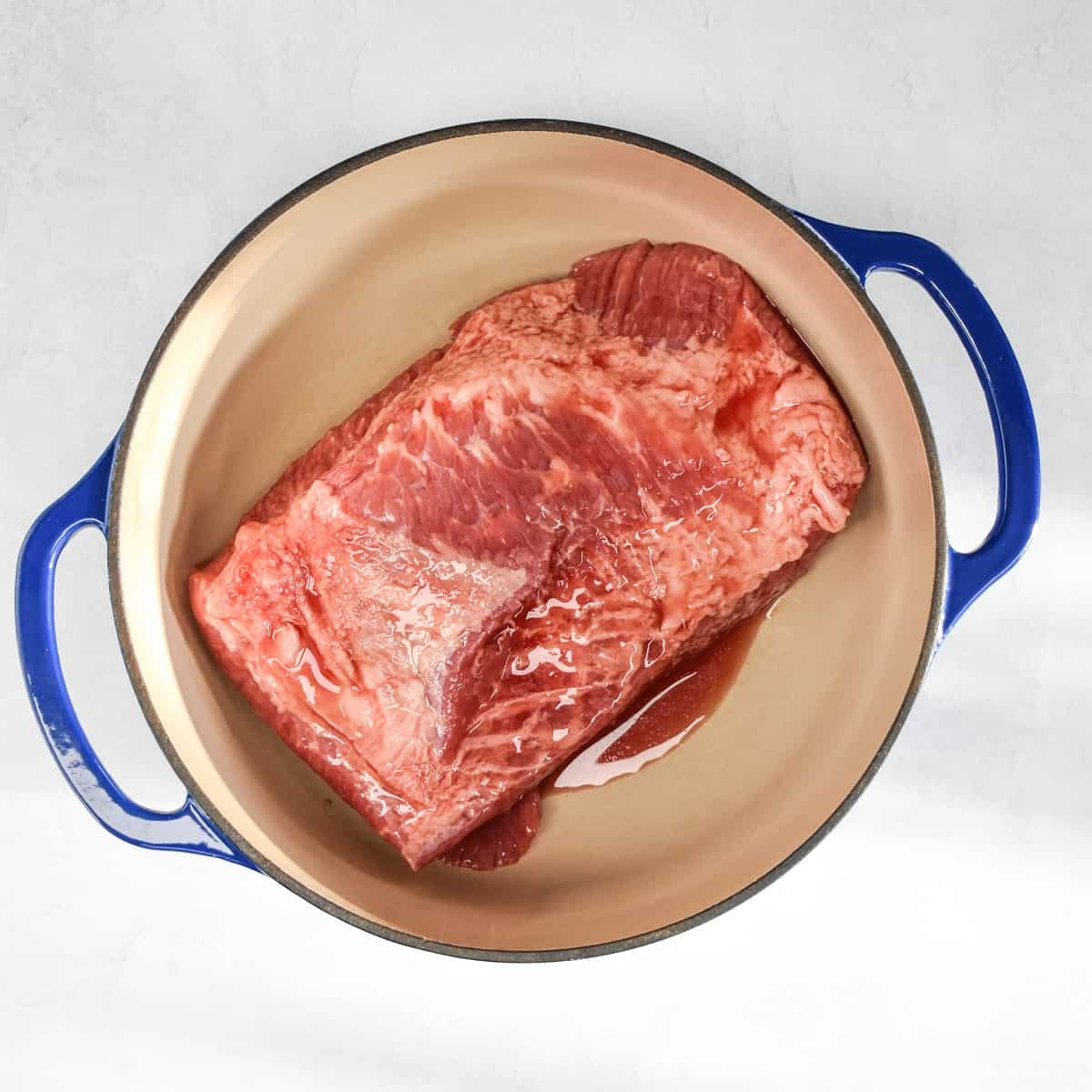 An image of the uncooked meat in a large, enameled Dutch oven.