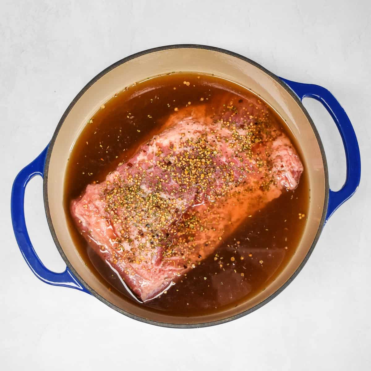The corned beef in a large pot with the seasoning on top and almost covered with beef broth and water.