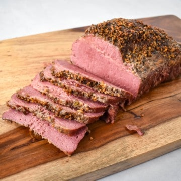 An image of the corned beef on a wood cutting board with half of it sliced.