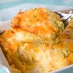 An image of a serving of the cheesy hash brown casserole held up by a large serving spoon over the baking dish.