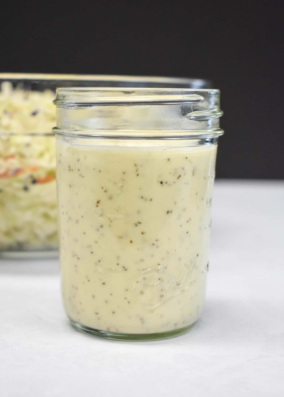 An image of the coleslaw dressing in a canning jar with a bowl of the cabbage in the background.