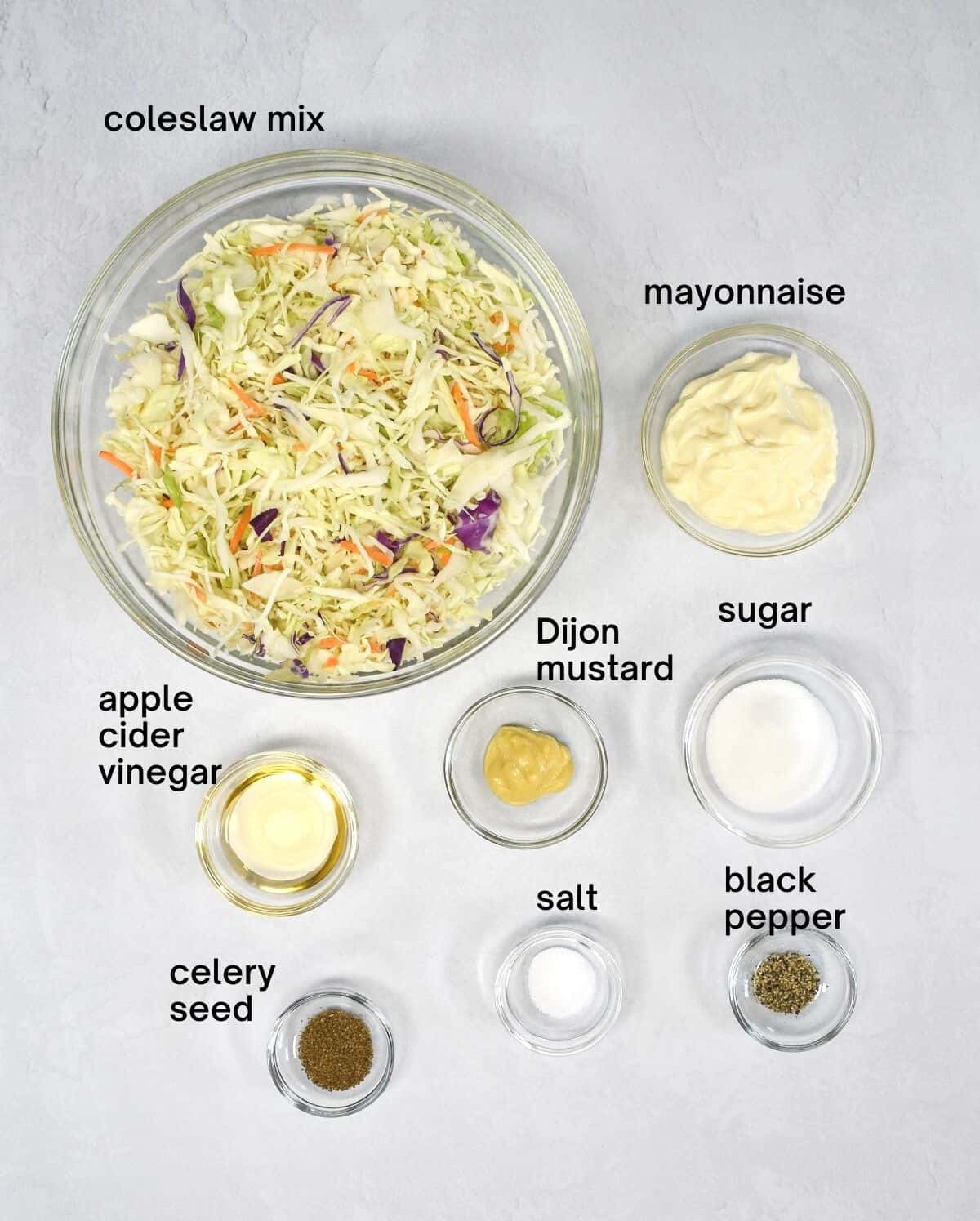 The ingredients for the easy coleslaw arranged in glass bowls on a white table.