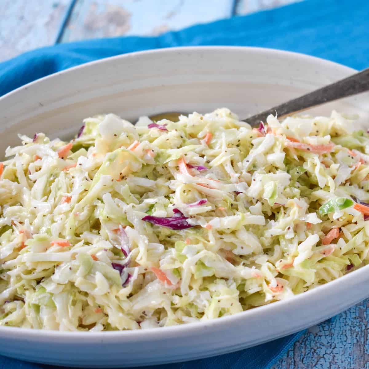 An image of the slaw served in an oval, white bowl that is set on an aqua linen.