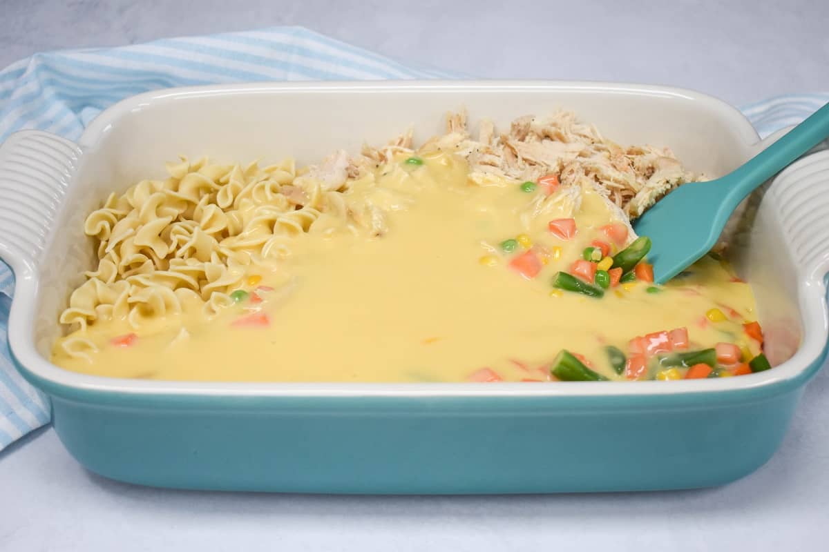 All the ingredients in a large baking dish before stirring, with a blue silicone spatula on the right side.