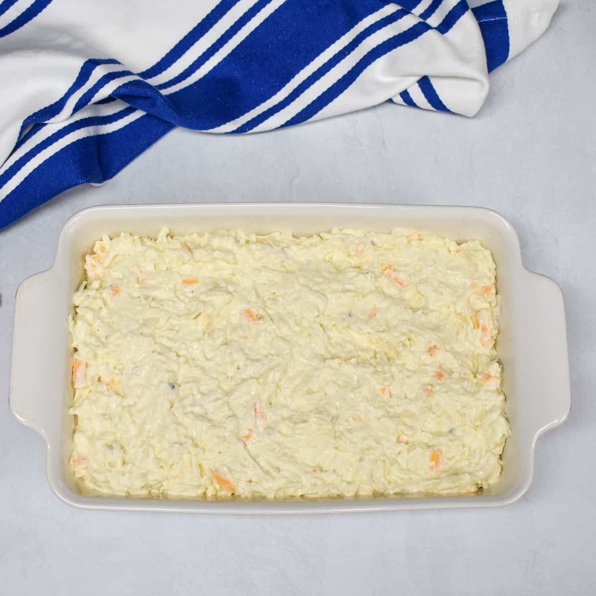 An image of the prepared mixture in a white casserole dish, set on a white table with a blue and white striped kitchen towel.