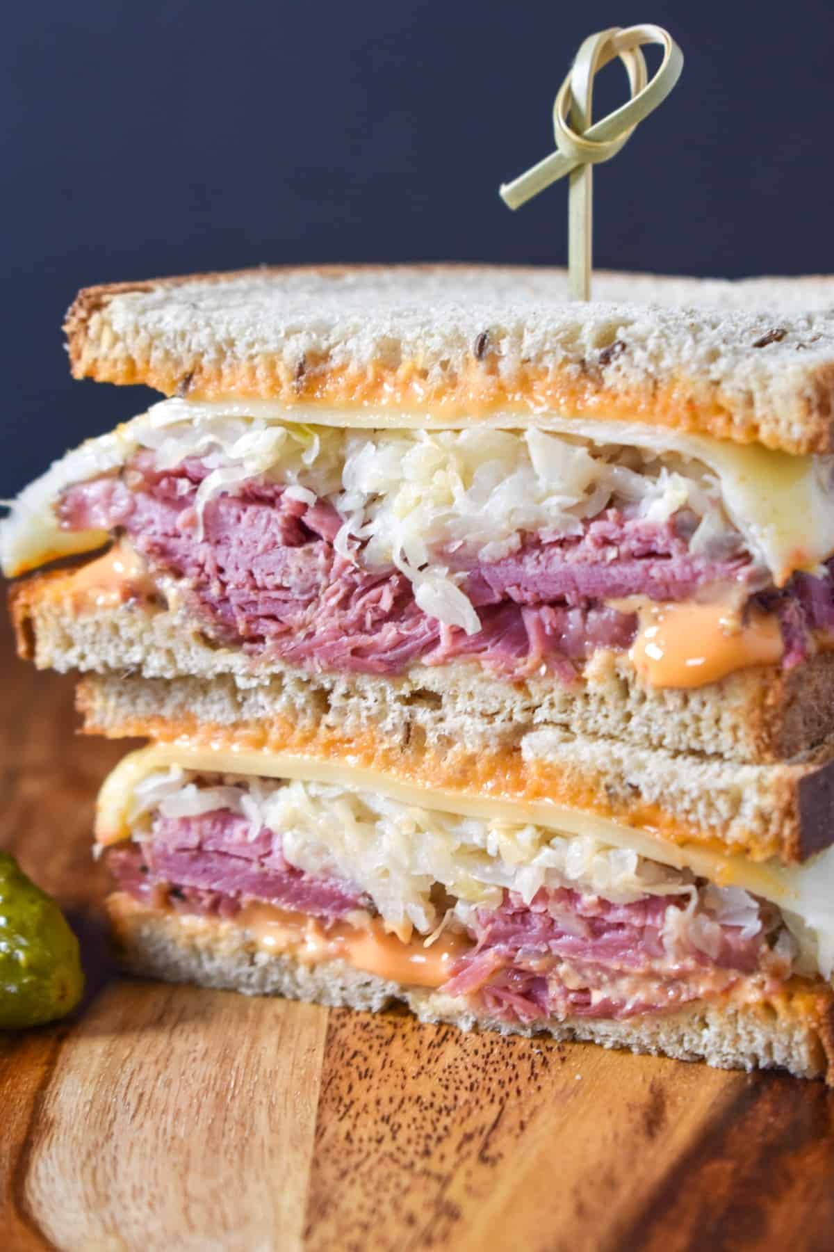 A close-up image of a Reuben sandwich, cut in half, stacked, and held together with a toothpick, set on a on a wood cutting board.