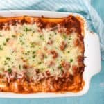 An image of the finished baked manicotti in a white baking dish set on a light blue table.