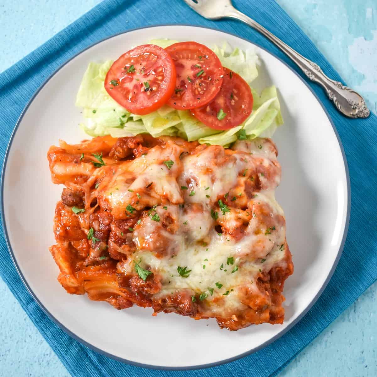 A serving of the pasta served with a side salad on a white plate that is set on an aqua linen.