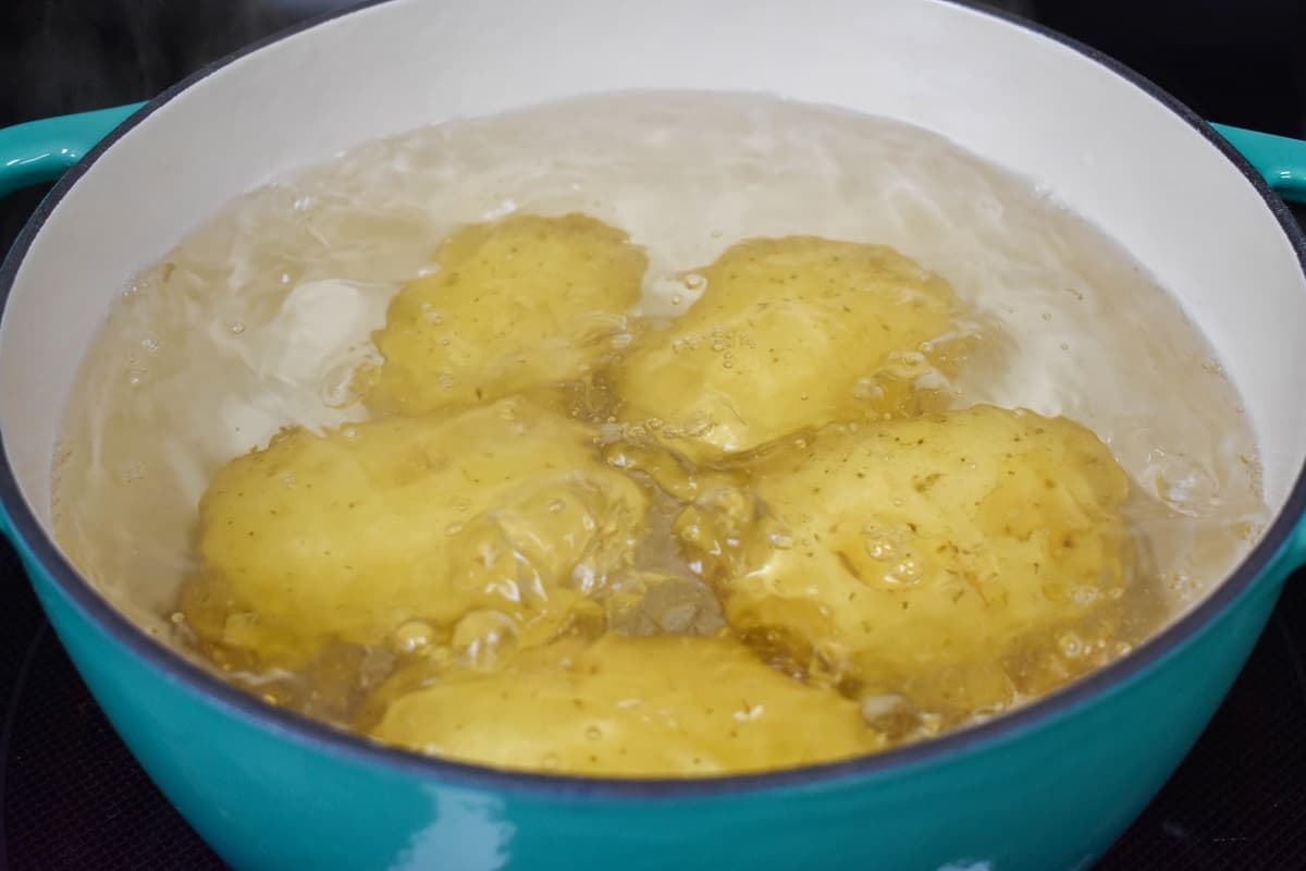 An image of five gold potatoes covered with water in a blue pot.