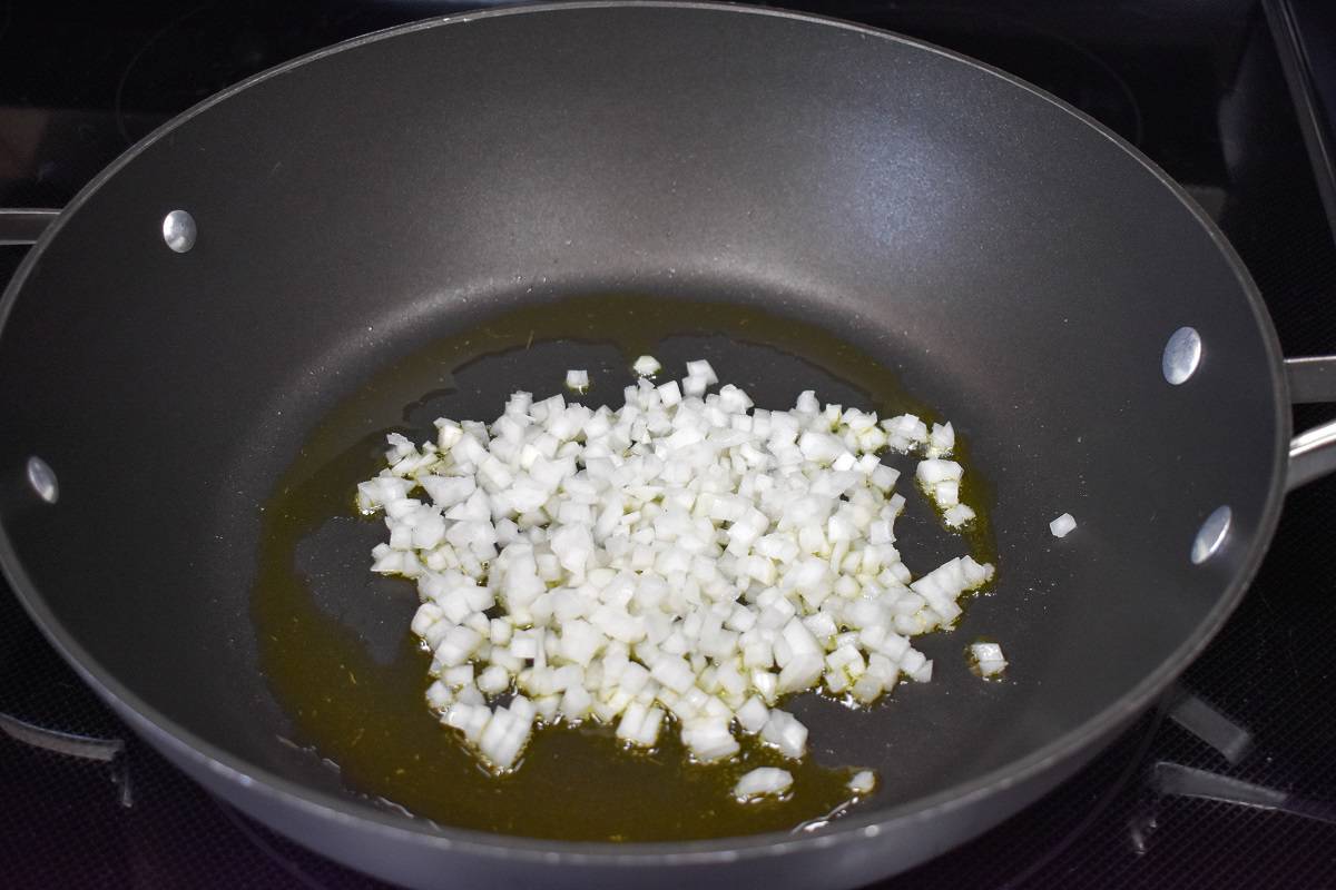 An image of diced onions cooking in a large, black skillet.