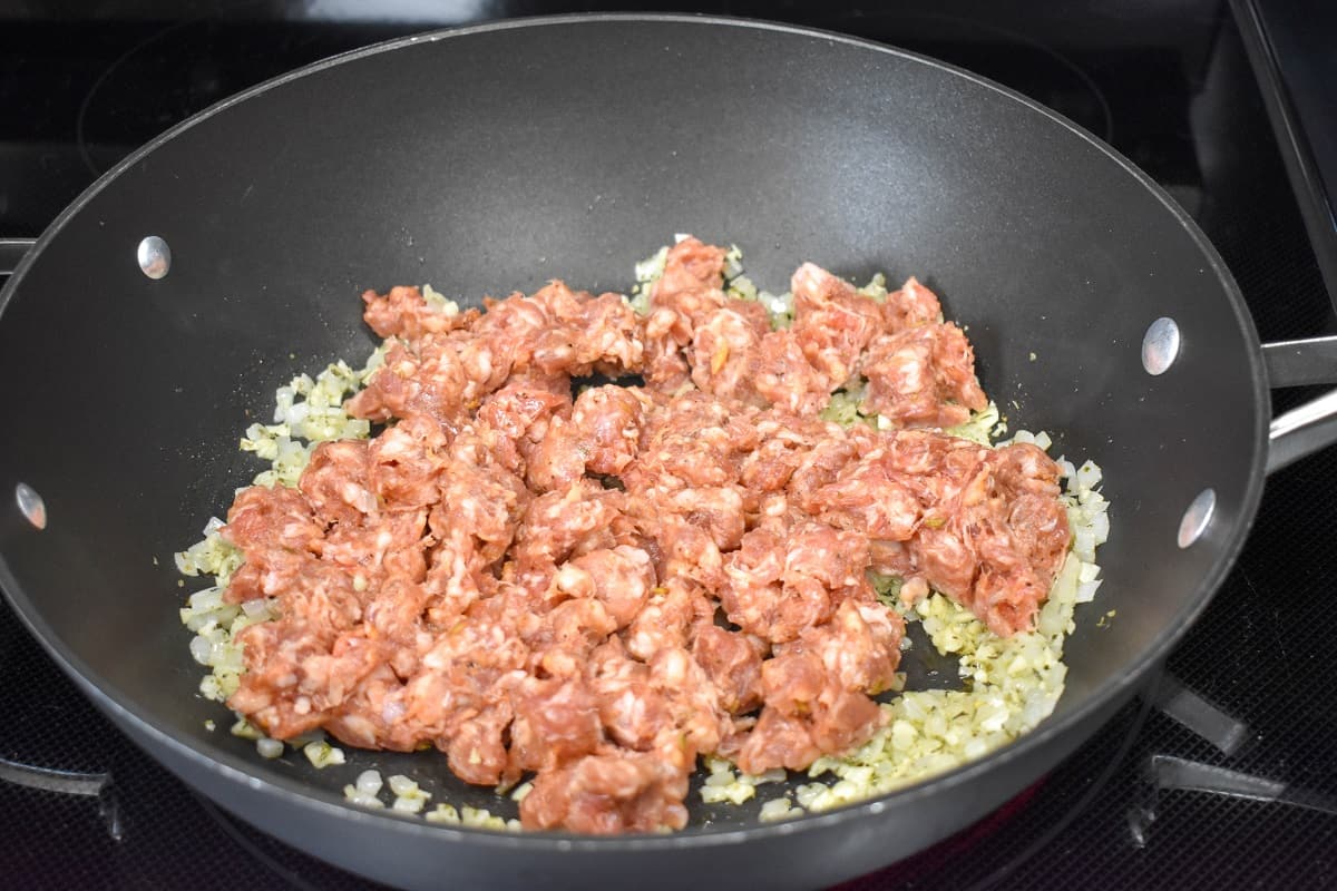 An image of Italian sausage added to the vegetables cooking in the skillet.