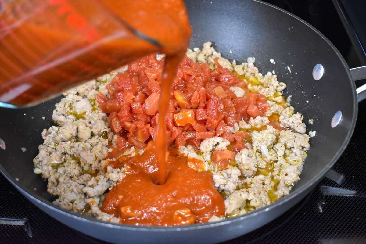 An image of pasta sauce being added to the skillet.