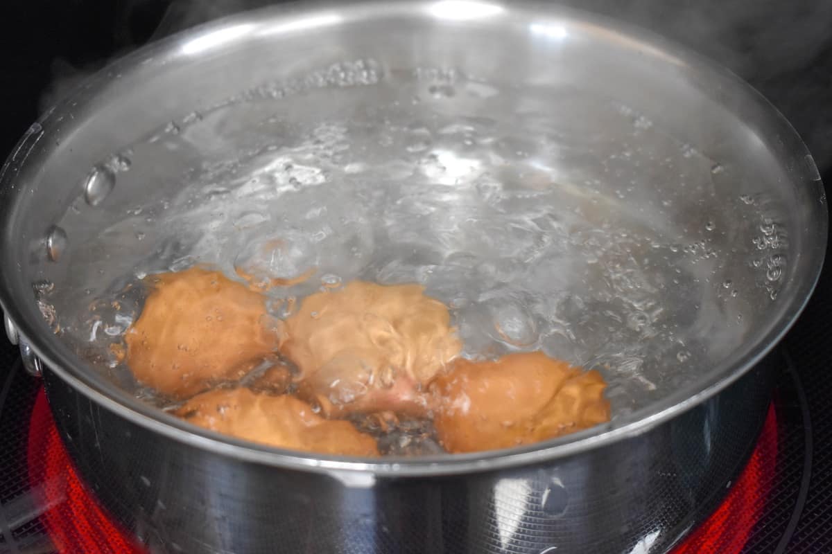 An image of four brown eggs boiling in a saucepan.
