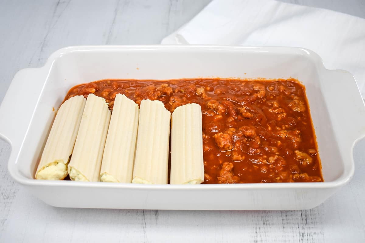 An image of a few manicotti set on the sauce in the white casserole dish.