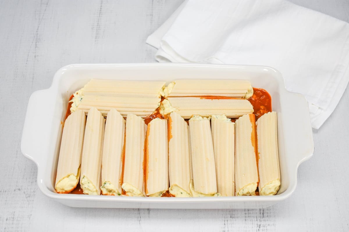 An image of the stuffed manicotti pasta arranged on the sauce in the baking dish.