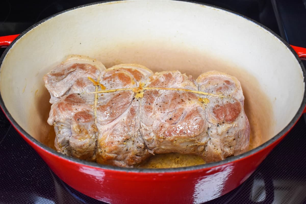 A large piece of pork shoulder, browned side up in a large pot.
