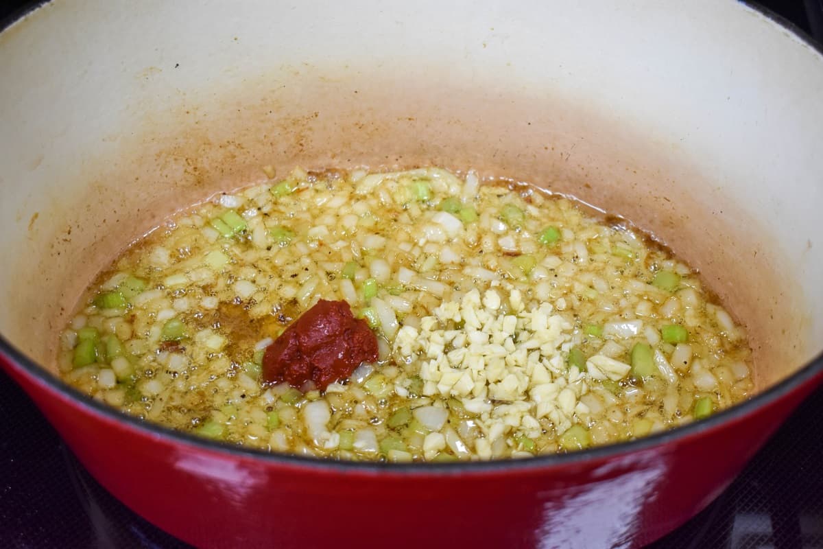 An image of minced garlic and tomato paste added to the sautéed onions and celery.