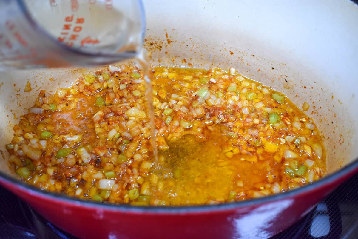 An image of white wine being added to the pot with the vegetables.