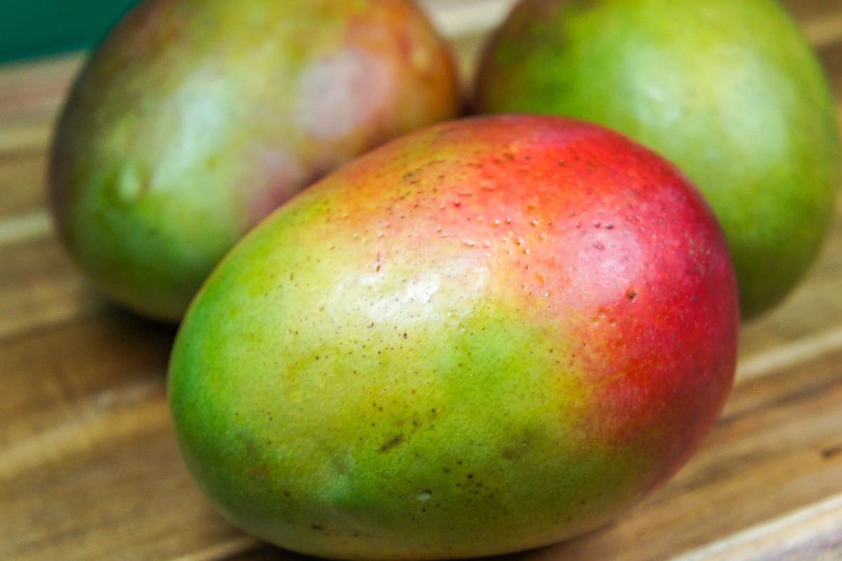 An image of three mangos on a wood cutting board.