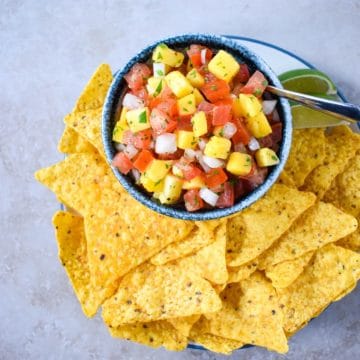 The mango salsa served in a small bowl and set on a plate with tortilla chips.