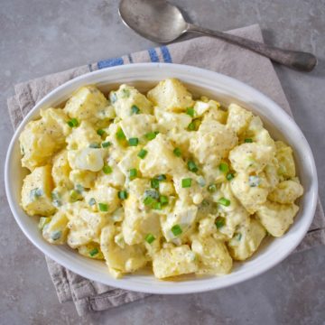 The potato egg salad served in a white bowl set on a beige and blue linen.