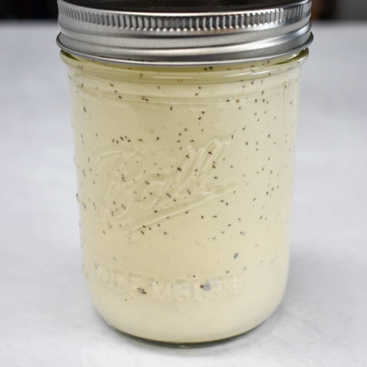 The dressing for the salad in a small glass jar set on a white table.