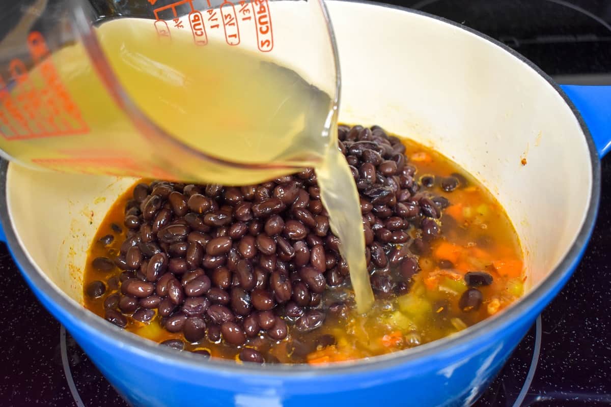 Chicken broth being added to the ingredients in the pot.