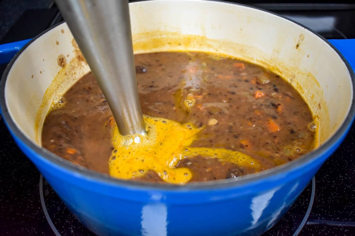 The soup being processed with an immersion blender in the pot.
