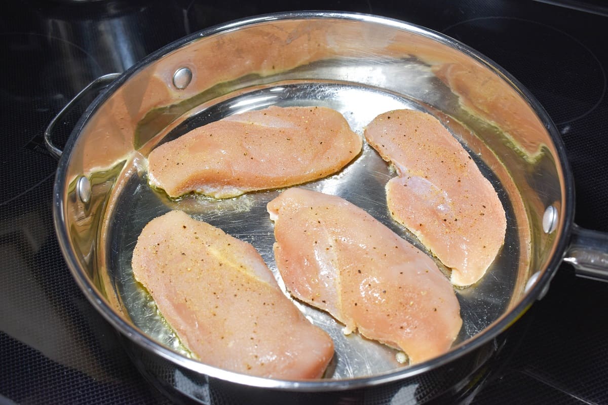 Four pieces of chicken breast cooking in a large skillet.