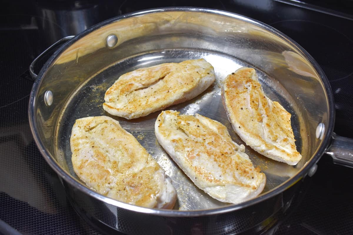 Four pieces of chicken breast cooking in a large skillet, browned side up.aking french onion chicken image 2