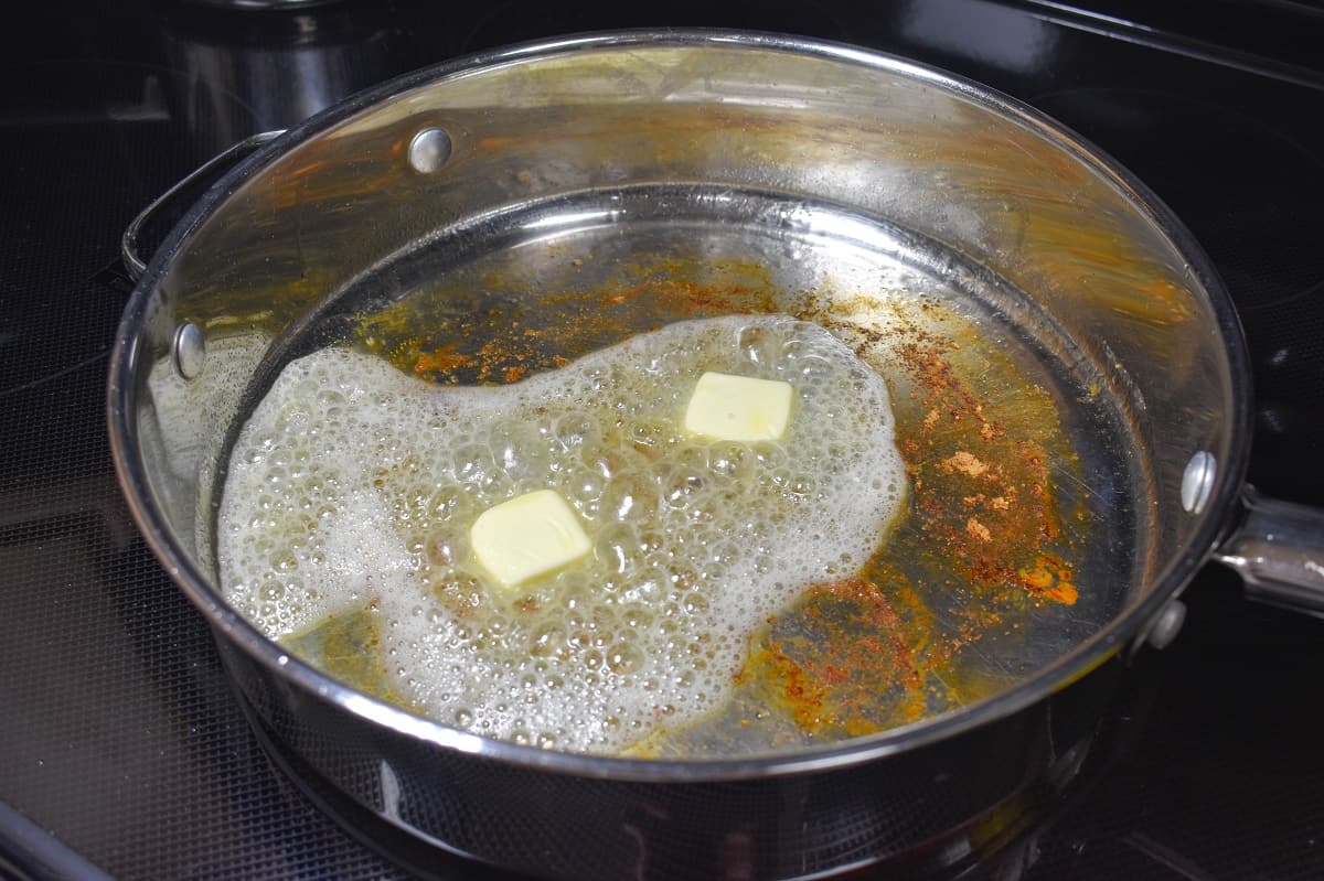 Two pats of butter melting in a large skillet with the caramelized bits from cooking the chicken.