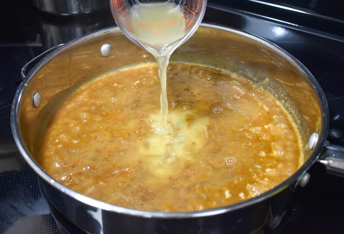 Chicken broth being added to the skillet with onions soup.