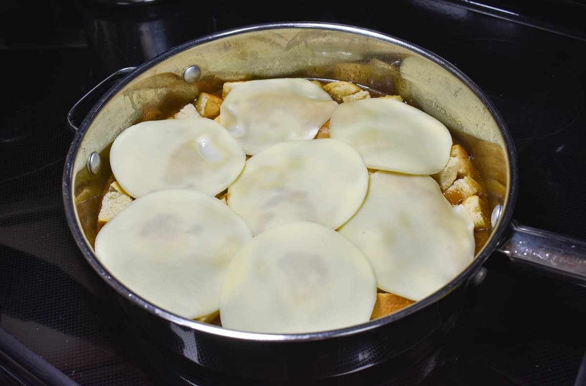 Round cheese slices placed over the ingredients in the skillet.