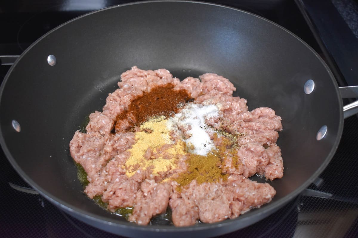 Ground turkey and spices in a large, black skillet.