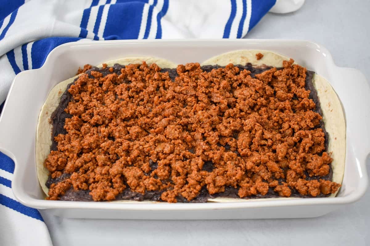 A layer of taco meat covering the ingredients in a white baking dish.key taco casserole image 11