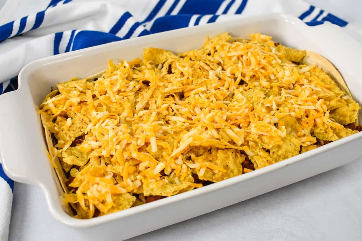 Tortilla chips arranged on the layered taco bake and topped with shredded cheese, before baking.