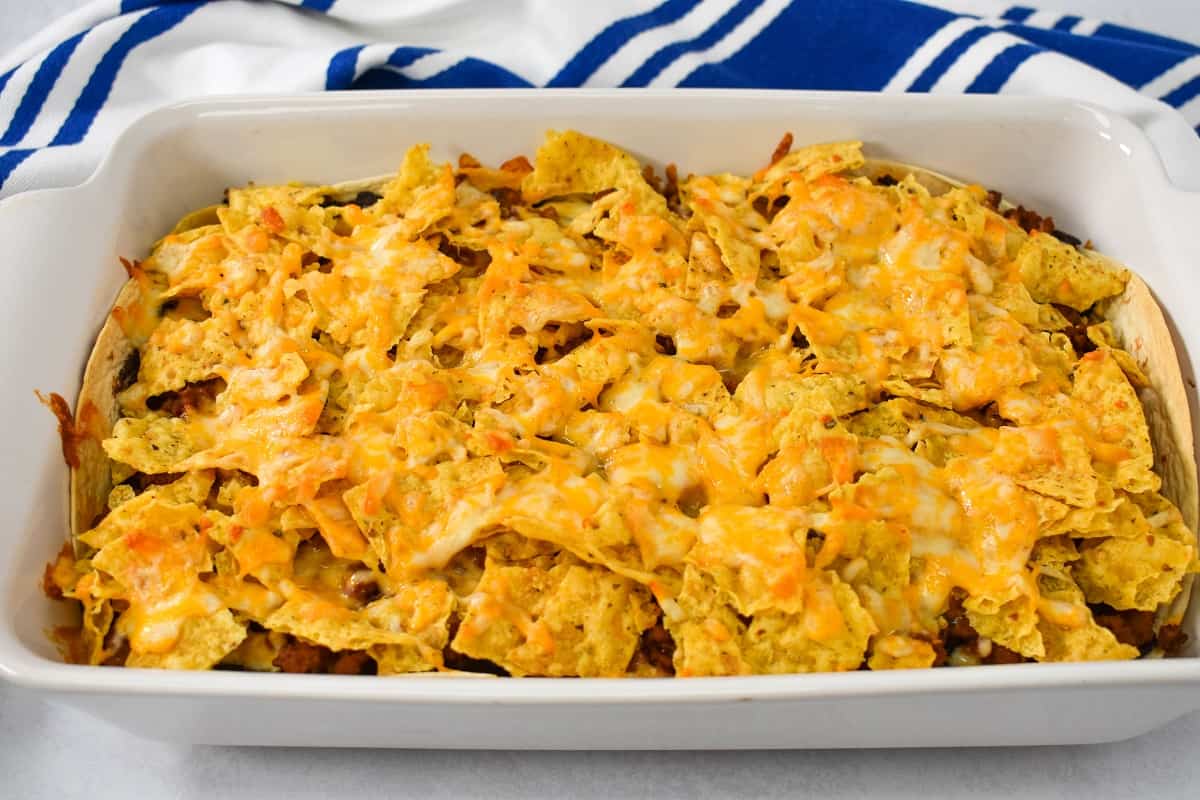 Tortilla chips arranged on the layered taco bake and topped with shredded cheese, after baking.