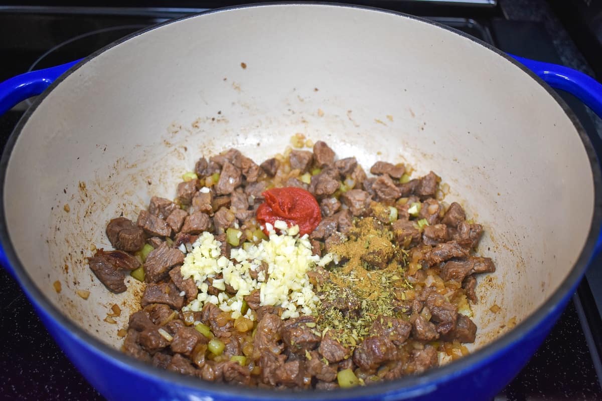 Garlic, tomato paste, and seasoning over browned steak pieces in a large pot.making vegetable beef soup image 3