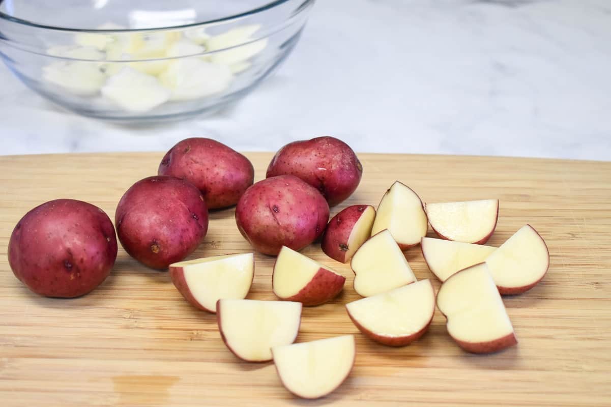 Whole and cut small red potatoes on a wood cutting board.