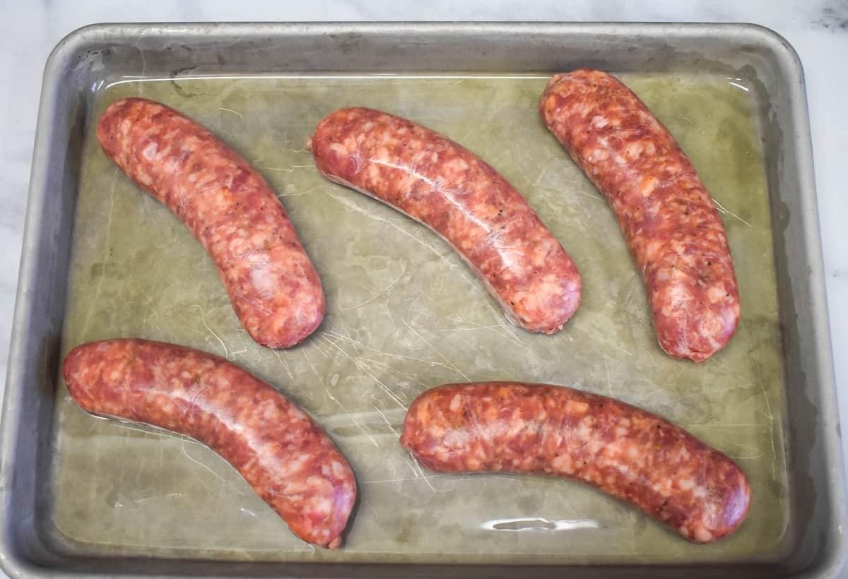 Five Italian sausages arranged on a greased sheet pan.