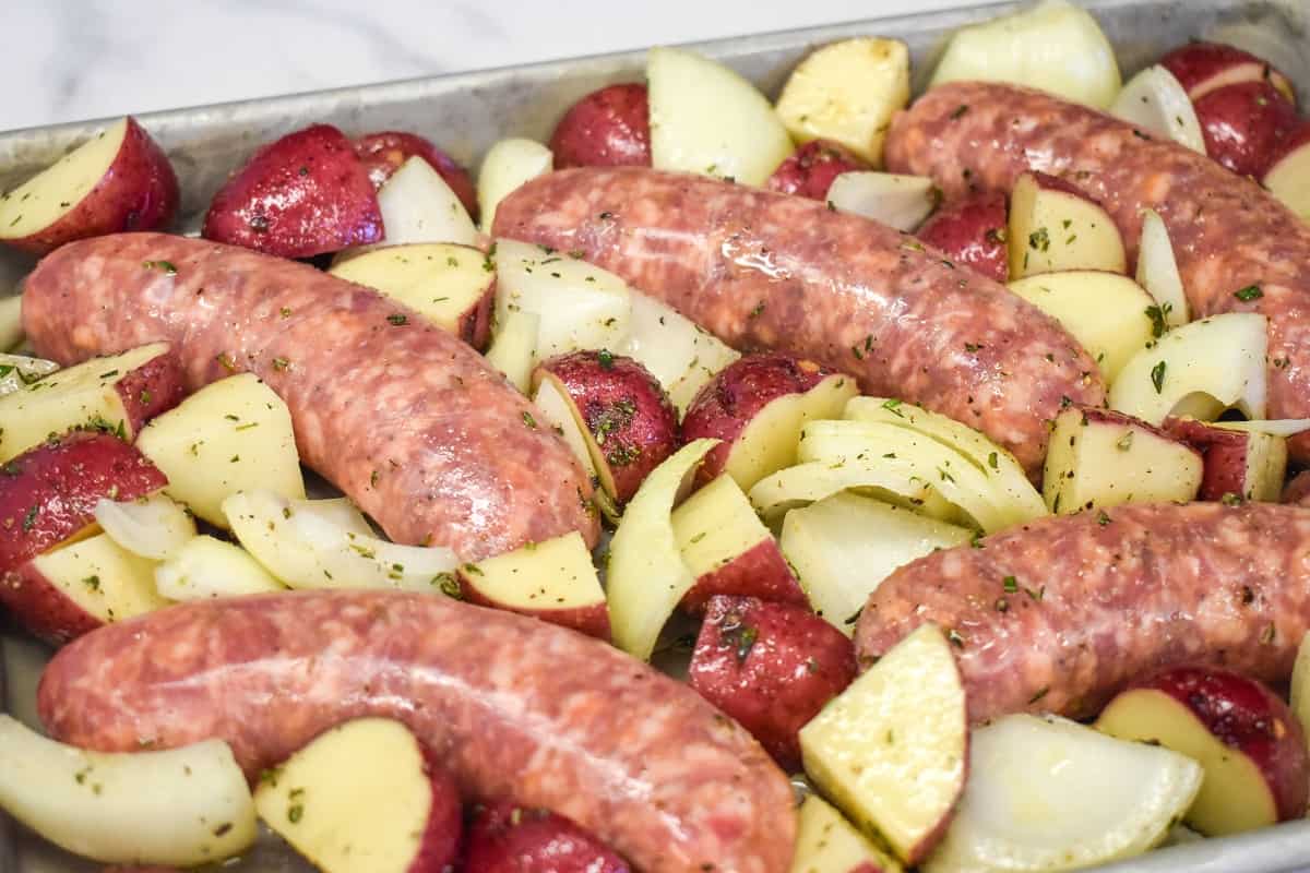 The Italian sausage with the potatoes and onion mixture arranged on a sheet pan.