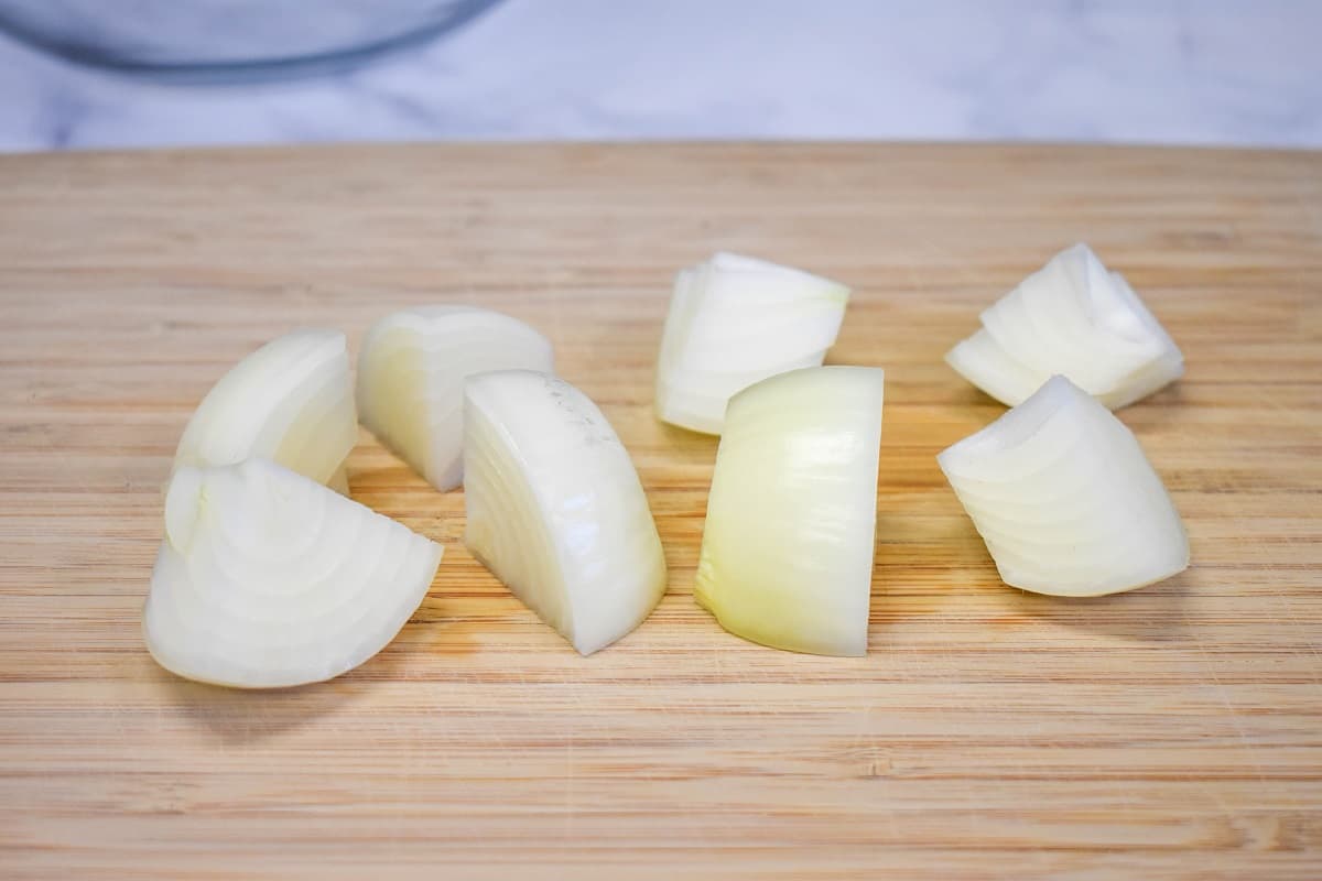 An onion cut into 8 pieces on a wood cutting board.